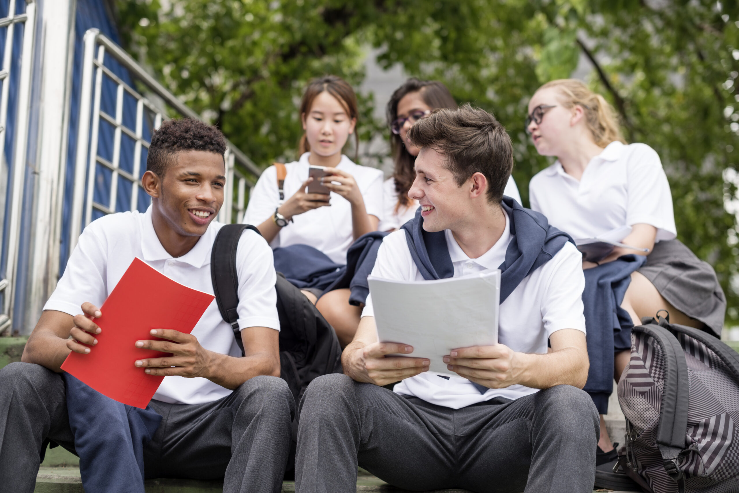 Group of students sat on steps outside at a school, dressed in uniform and all talking amongst themselves