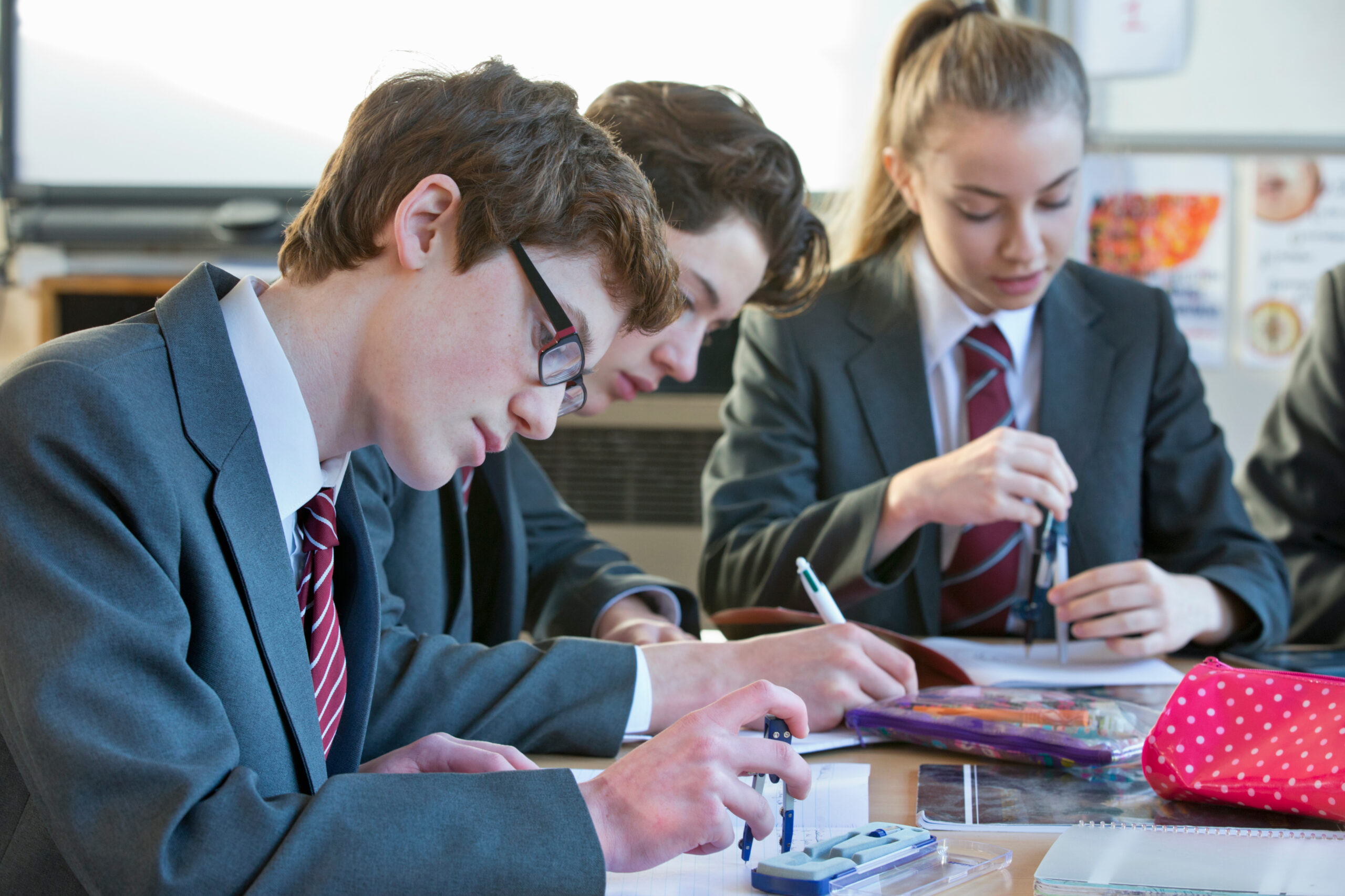 Three students sitting using compasses in a math class, all are focused on their work